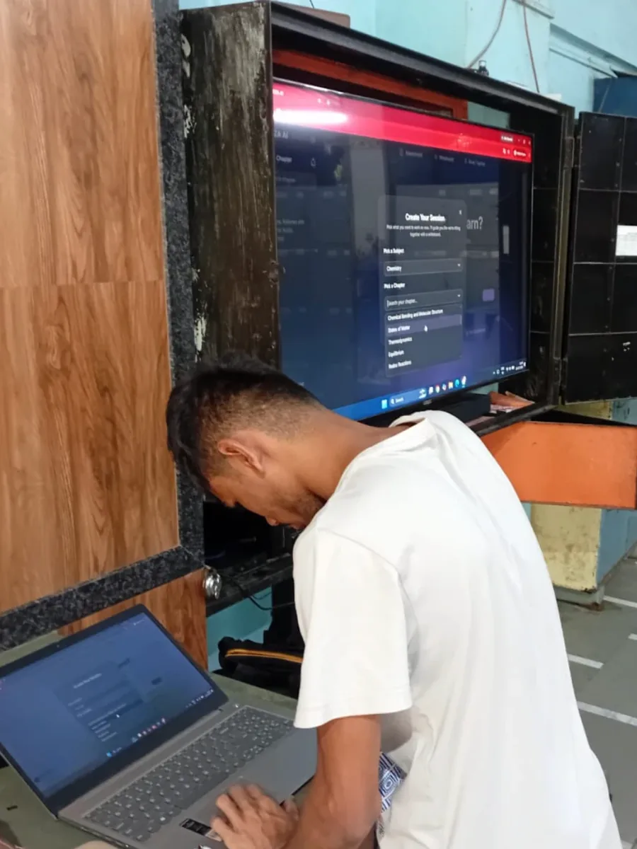 An Avana learner working on a laptop beside a large screen during a session